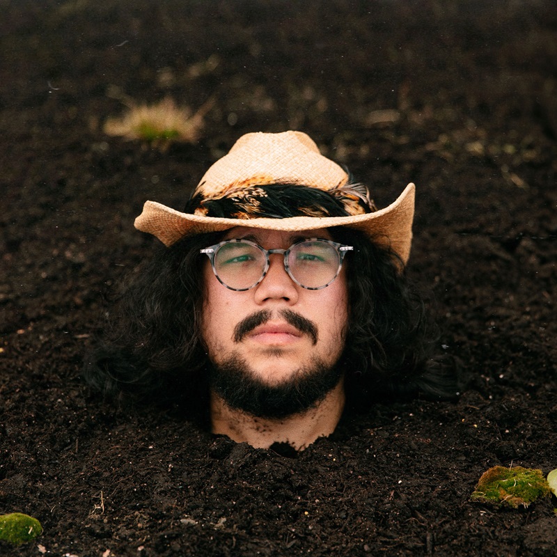 Bearded young man with Asian features buried to his neck in fresh earth