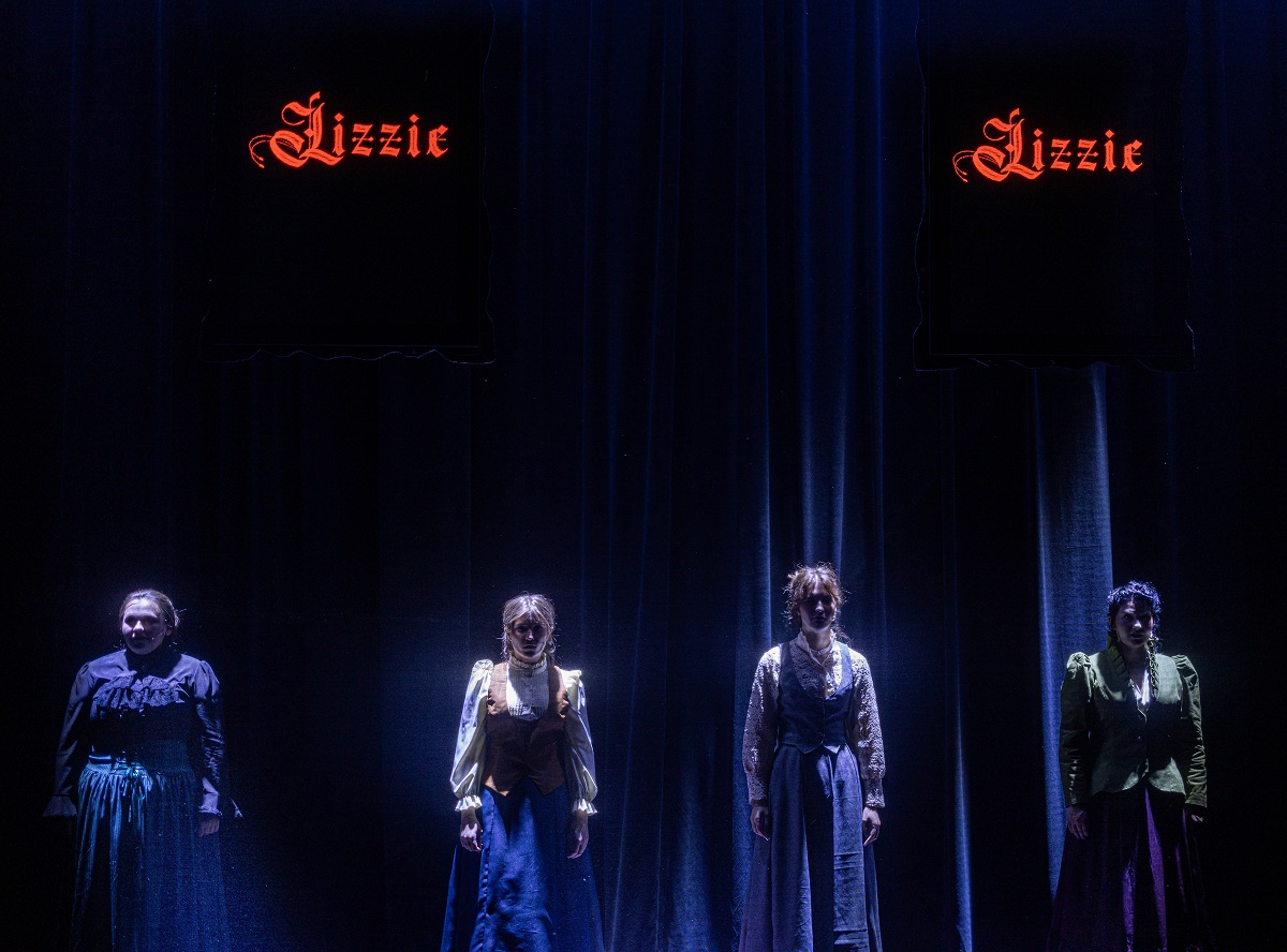 4 women in Victorian dress beneath signs reading "Lizzie"