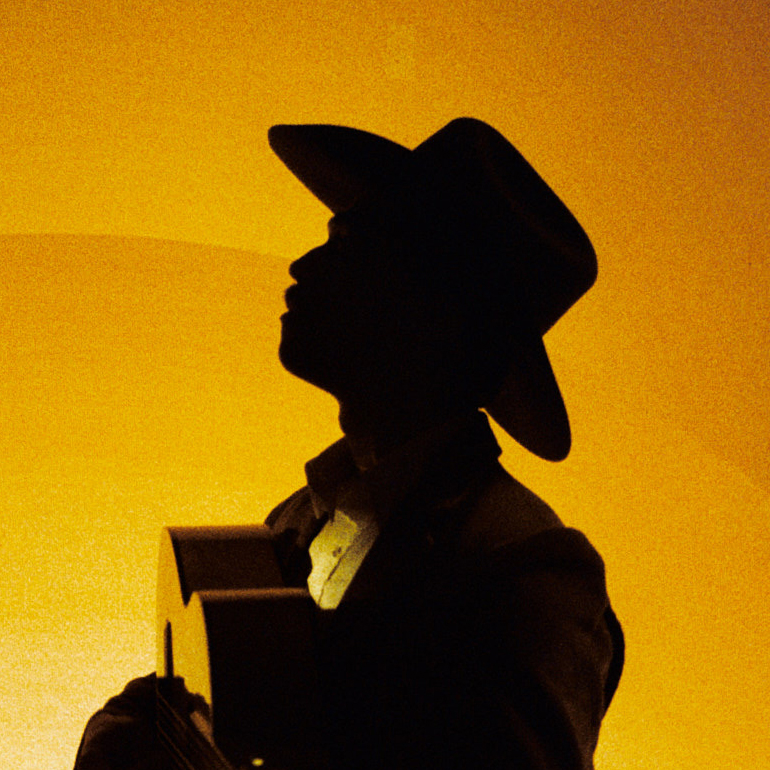 Half-profile of man in cowboy hat playing acoustic guitar in silhouette