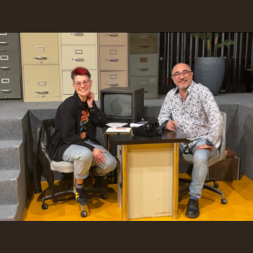 Director Ashley Kelly Tata seated on office set opposite interviewer Stewart Ikeda