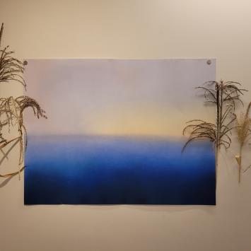 Mixed media blue painting surrounded by dried grasses