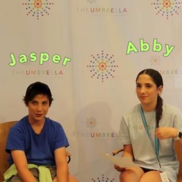 Teenage siblings named Jasper and Abby site smiling in front of a backdrop with The Umbrella and colorful brandmark against a white background