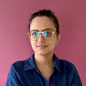 Female artist with glasses in blue shirt against a rose backdrop